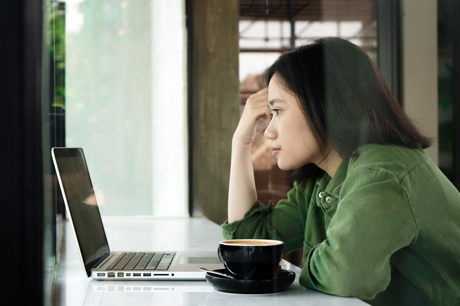 A tired young professional resting her head on her hand at her laptop